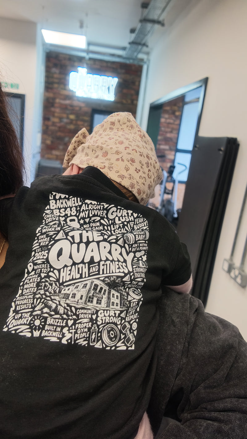 A child being carried at The Quarry, wearing a Quarry artwork T-shirt beneath the gym sign.