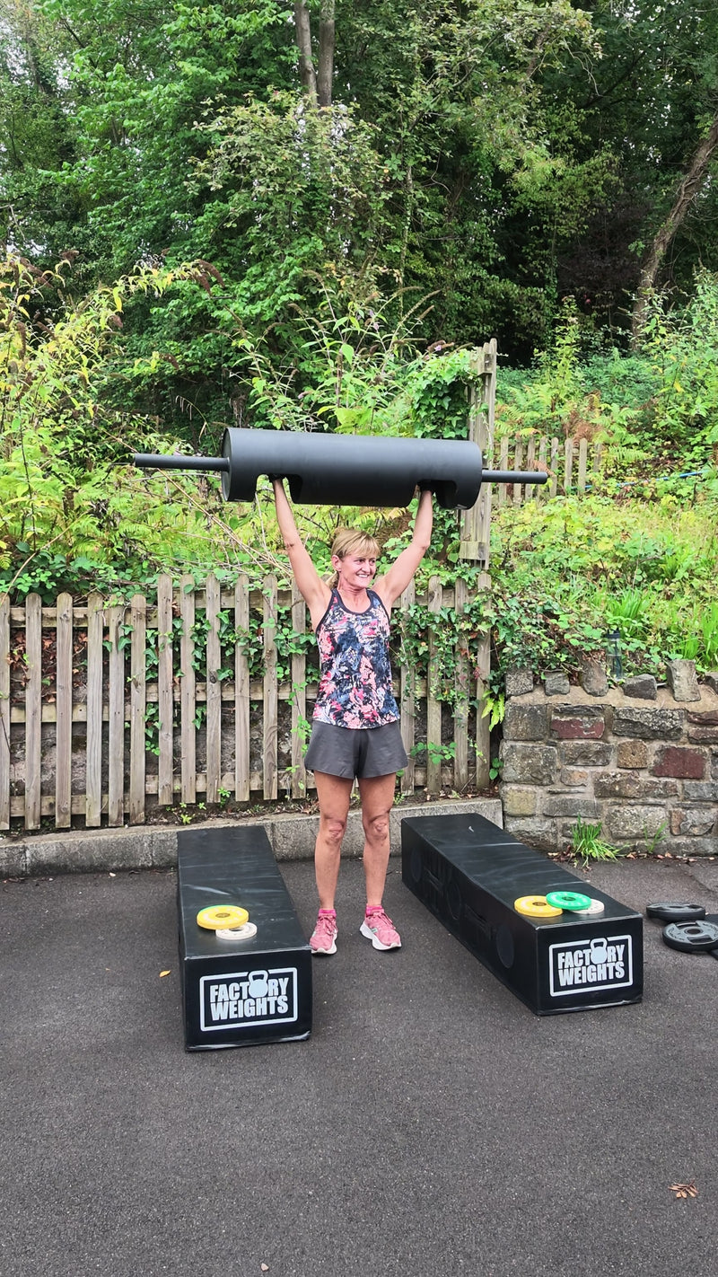 A smiling member lifting a training log in The Quarry outdoor area.